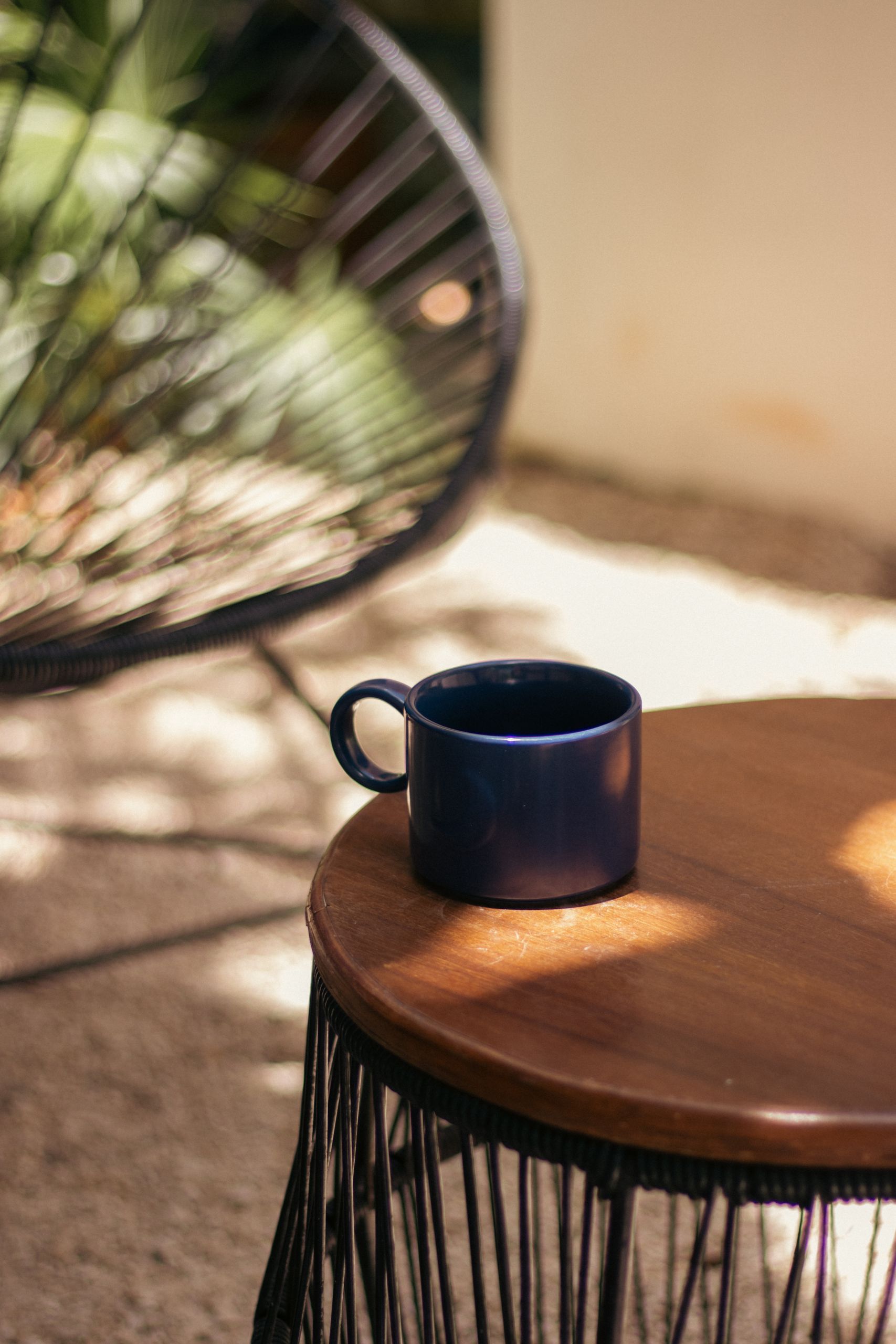 A tranquil scene with a blue coffee cup on a round wooden table in sunlight.