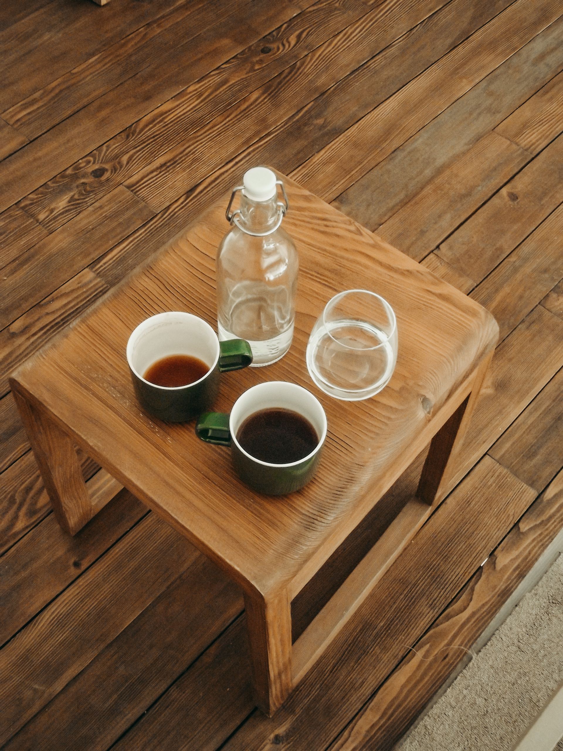 High-angle view of a wooden table with two coffee cups and a glass bottle.
